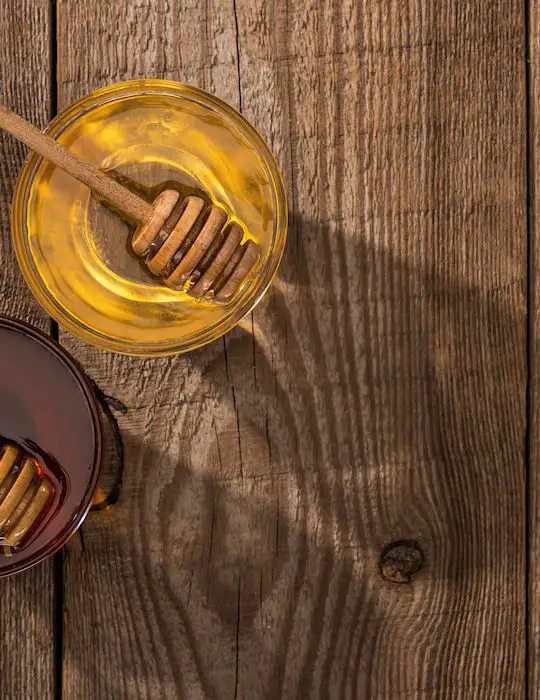 top view of jars with honey and honey dippers on wooden table in sunlight