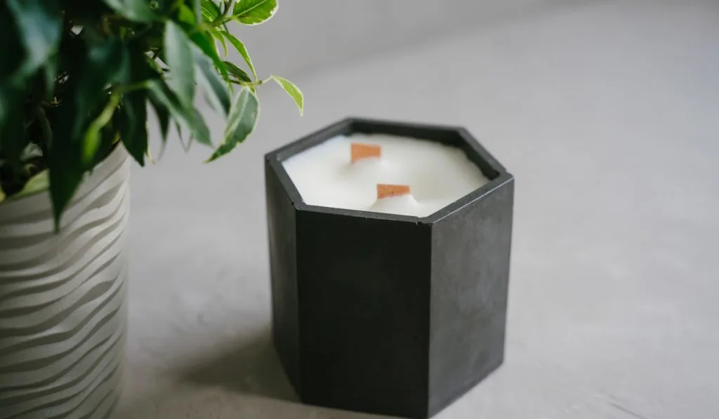 A candle made of natural soy wax in a black geometric plaster candlestick.

