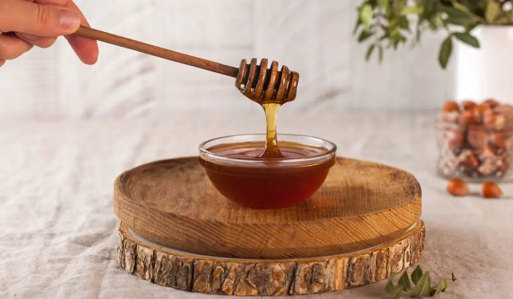 Brown honey in a glass bowl on a rustic wooden board