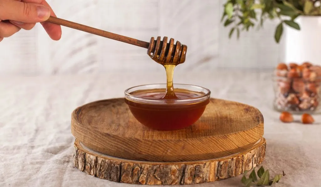 Brown honey in a glass bowl on a rustic wooden board