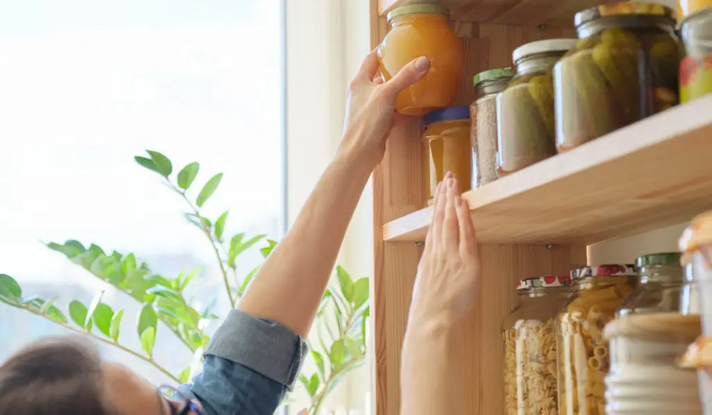 Food products in the kitchen storing ingredients in pantry. Woman putting jar of honey