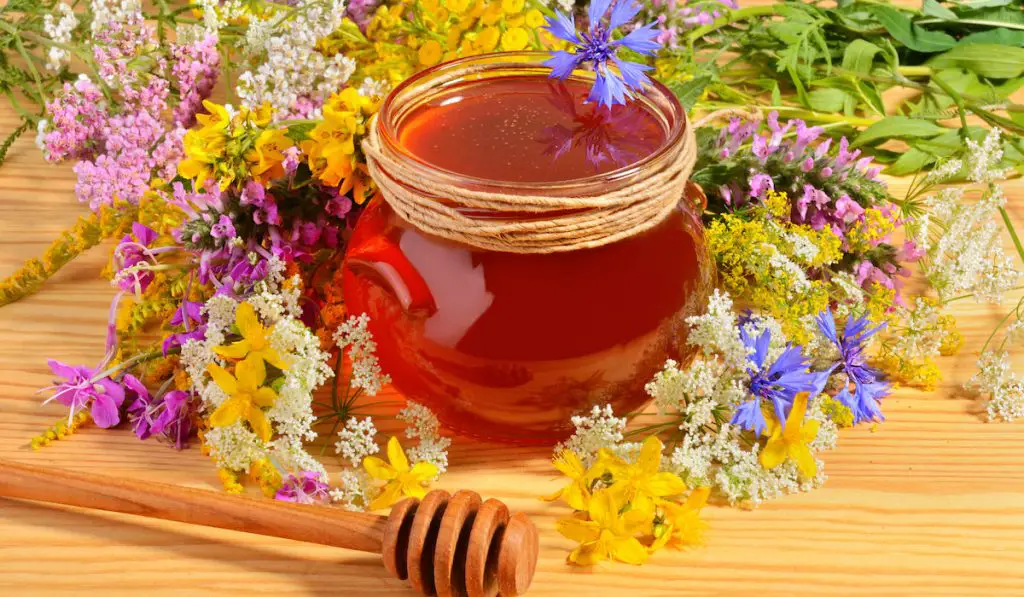 Glass pot of sweet honey with flowers on wooden table

