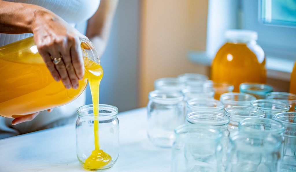 Woman pours honey into transparent jars on a white table
