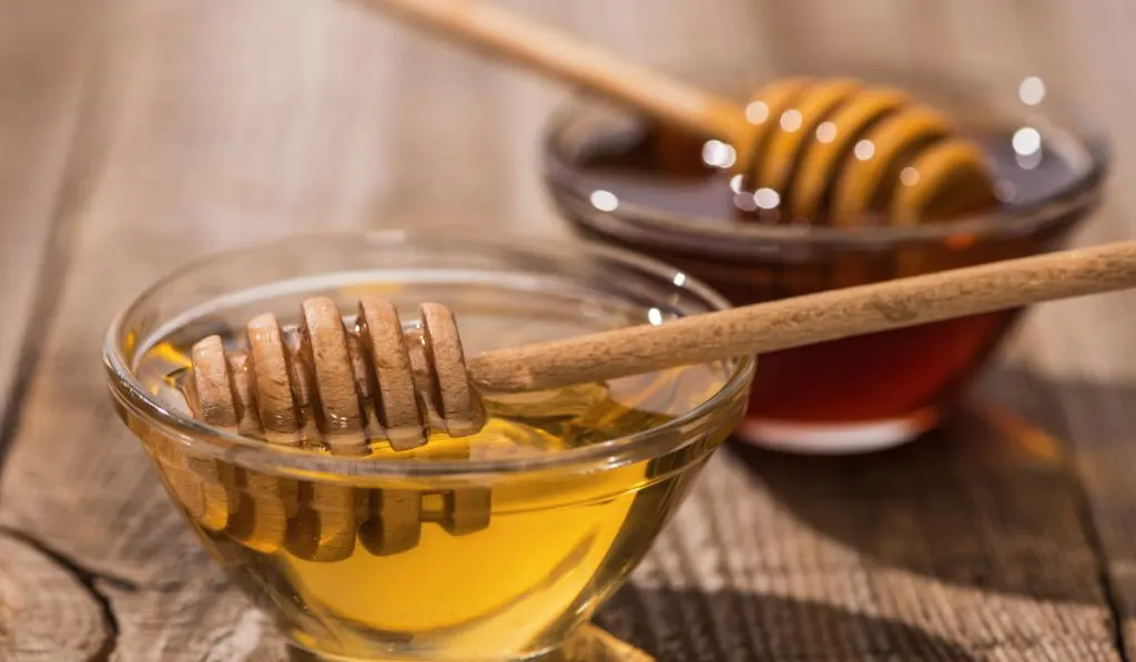 two bowls of honey with dippers on wooden table