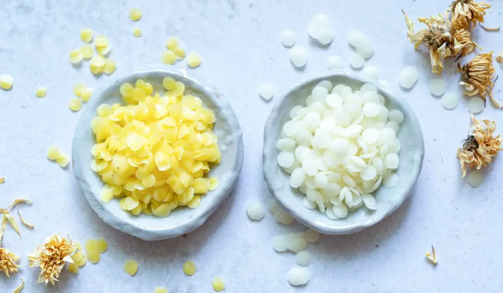 yellow and white cosmetic beeswax pellets in white ceramic bowl